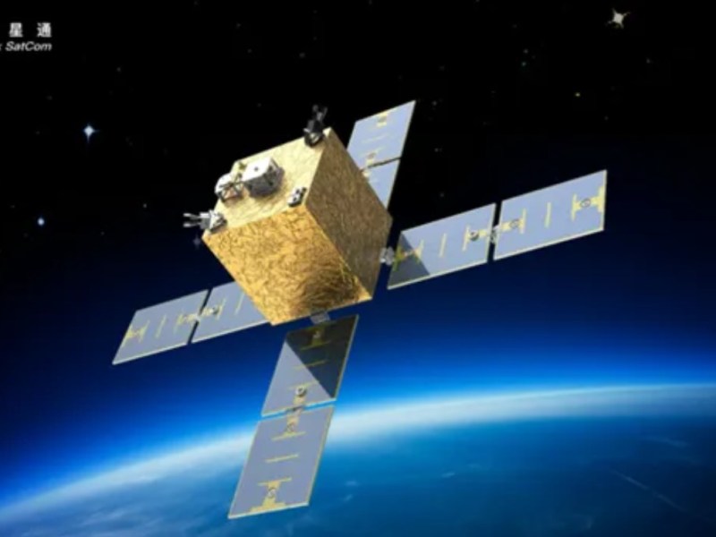 Render of a Bluelink Satcom satellite in low Earth orbit, featuring a gold-colored cube-shaped bus with four extended solar panel arms arranged in a cross configuration, set against the backdrop of space and the Earth's horizon.