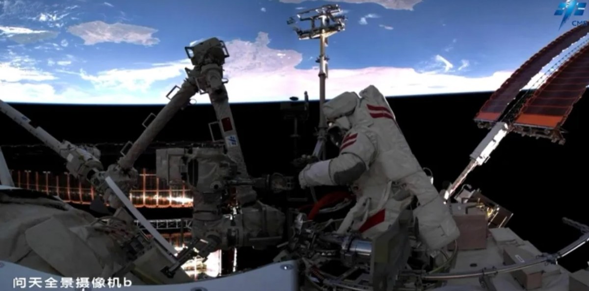 A Chinese astronaut conducts a spacewalk outside the Tiangong space station, working on the robotic arm while Earth is visible in the background. The scene was captured by a panoramic camera on the Wentian module during Shenzhou-20’s second EVA on June 26, 2025.