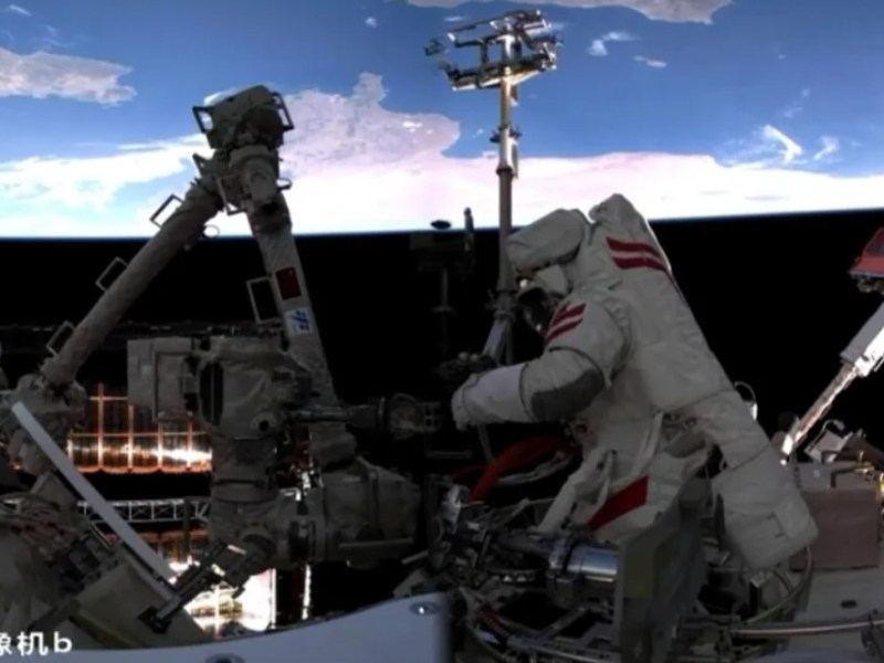 A Chinese astronaut conducts a spacewalk outside the Tiangong space station, working on the robotic arm while Earth is visible in the background. The scene was captured by a panoramic camera on the Wentian module during Shenzhou-20’s second EVA on June 26, 2025.