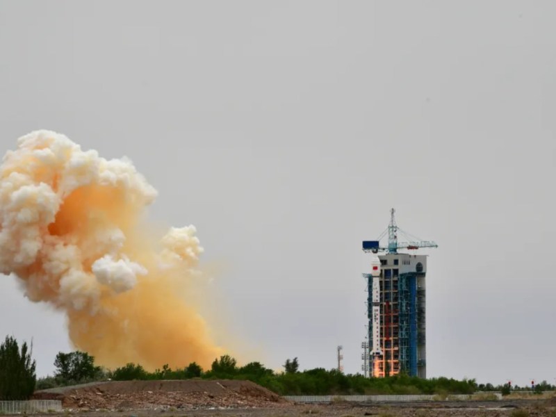 A Long March 4B rocket lifts off from the Jiuquan Satellite Launch Center in northwest China on May 29, 2025, carrying the classified Shijian-26 satellite. A large plume of orange and white smoke billows to the left of the launch pad under an overcast sky.