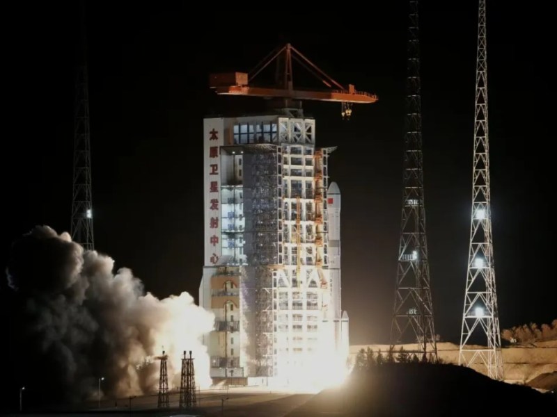 A Long March 6A rocket lifts off at night from the Taiyuan Satellite Launch Center, China, with bright exhaust and smoke plumes illuminating the launch pad tower bearing Chinese characters.