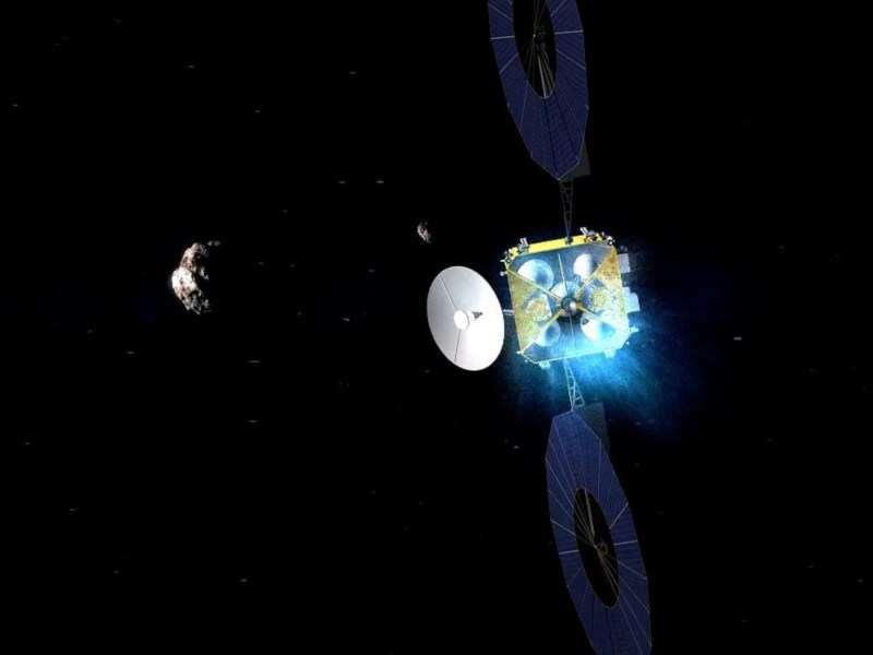An artistic rendering of China's Tianwen-2 spacecraft approaching an asteroid in deep space. The probe features large circular solar panels, a dish antenna, and an ion propulsion system emitting a blue glow. A small asteroid is visible in the background, set against the vast darkness of space.